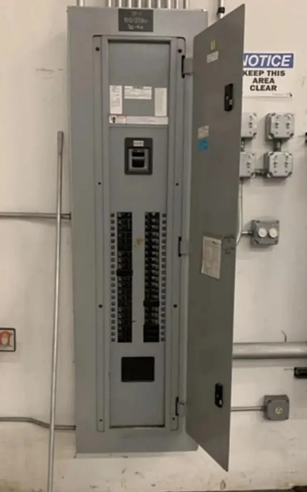 Open electrical panel with breaker rows and a caution notice, serviced by AM Electrical